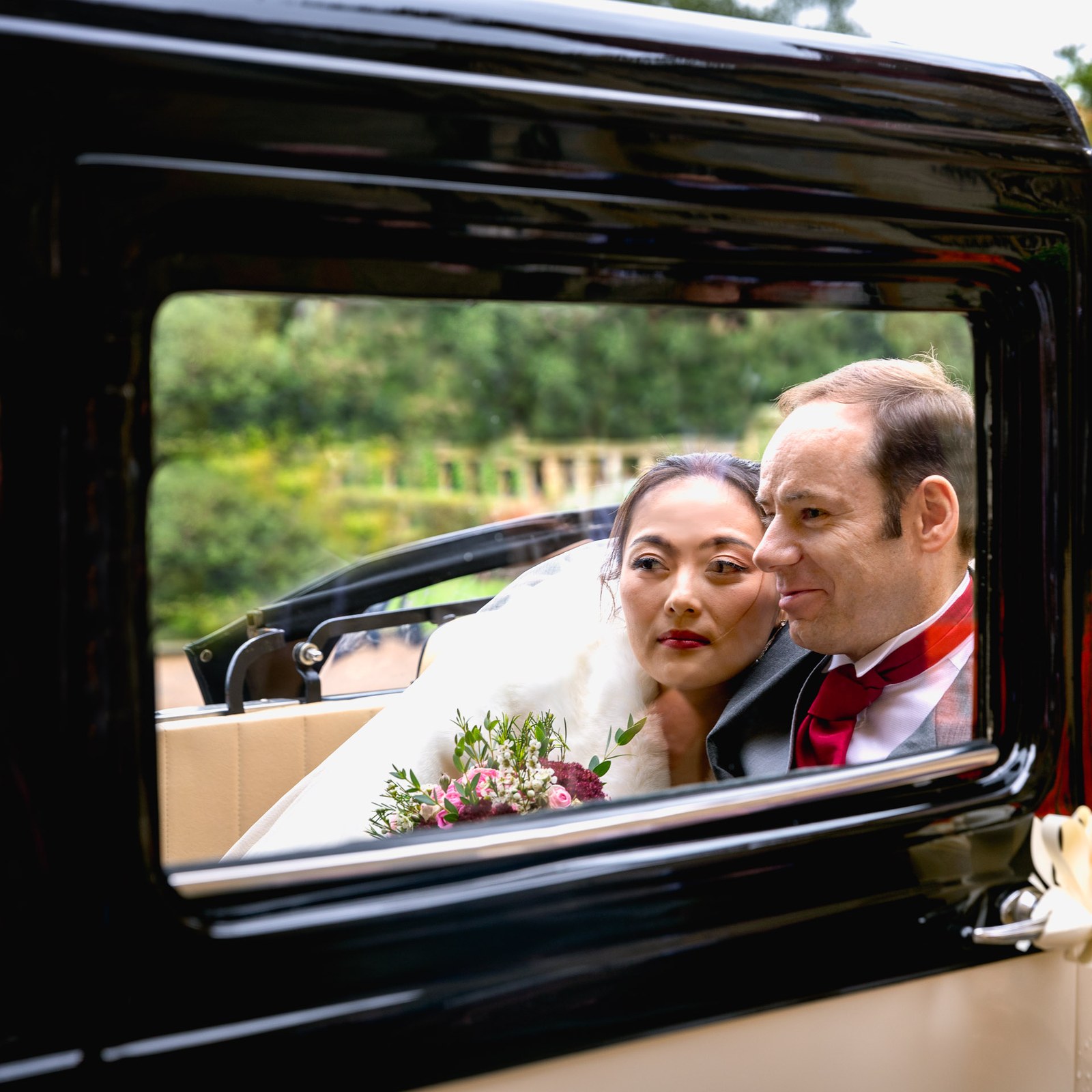 Bride and groom looking out through the window of the vintage wedding car