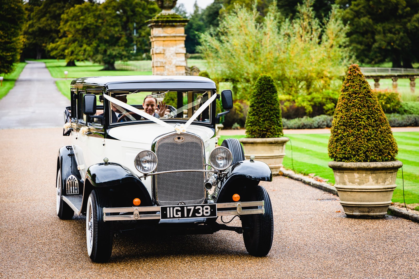 The ribboned vintage car sweeping up the tree-lined drive to Eynsham Hall
