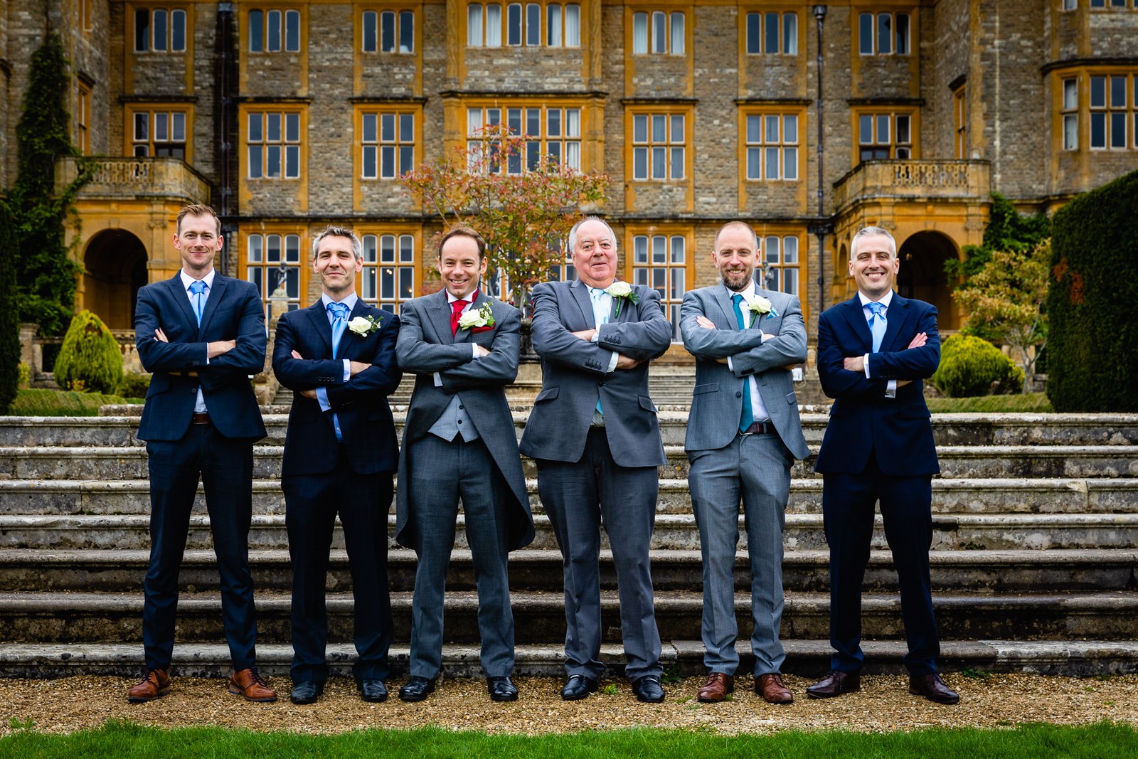 The groom and his groomsmen lined up with folded arms before the steps at Eynsham Hall