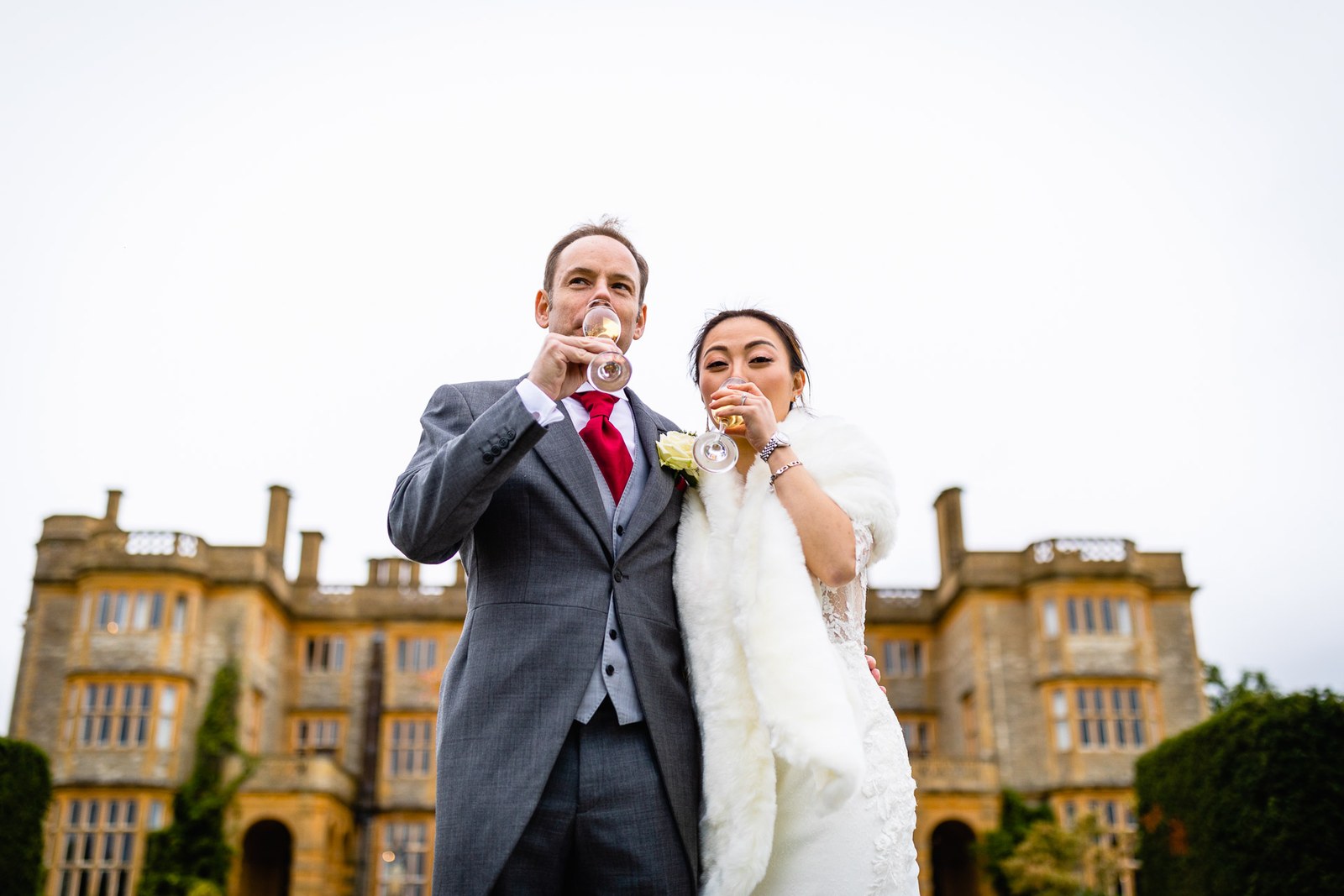 Bride and groom sipping champagne side by side before the walls of Eynsham Hall