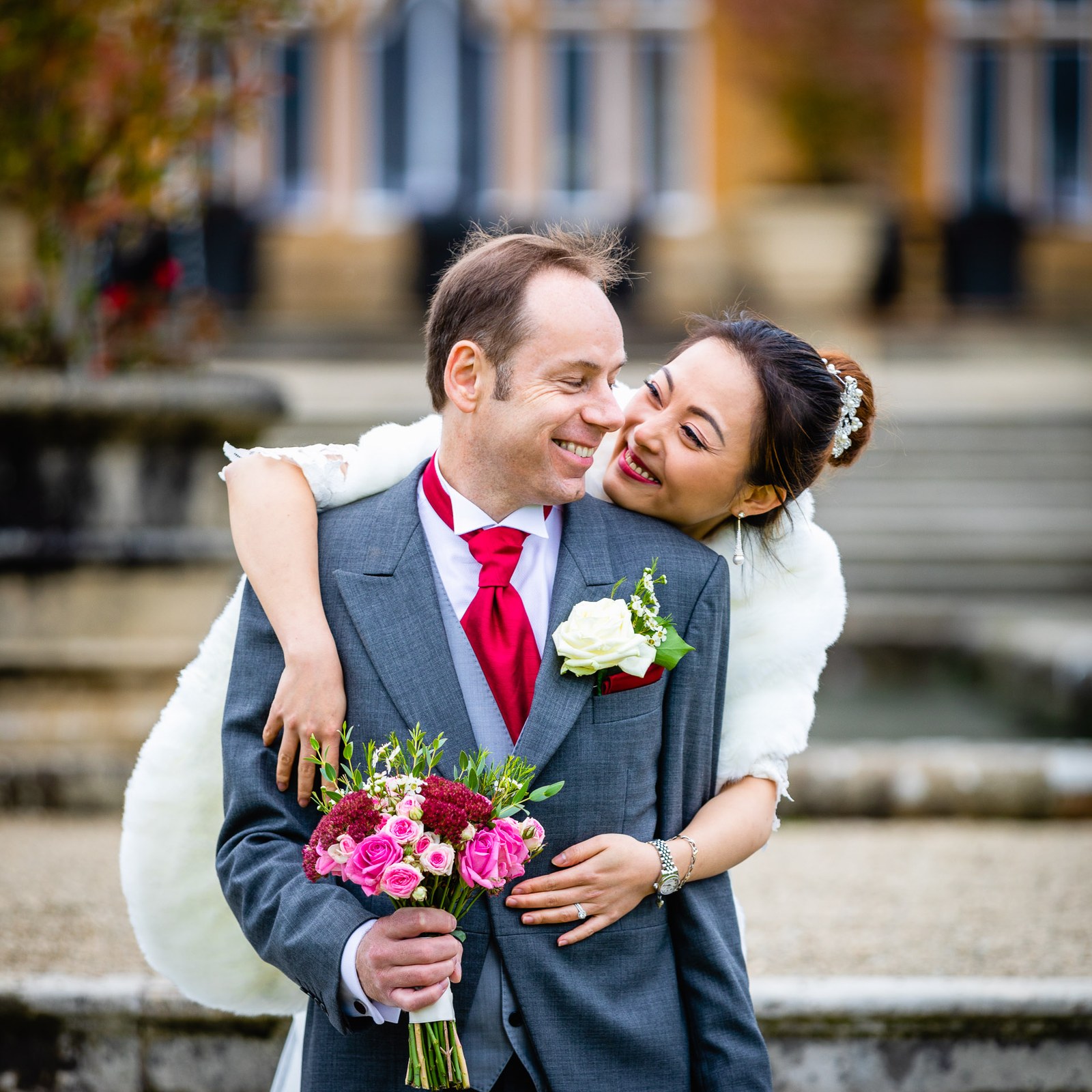 The couple embracing on the terrace, the mullioned windows of Eynsham Hall behind