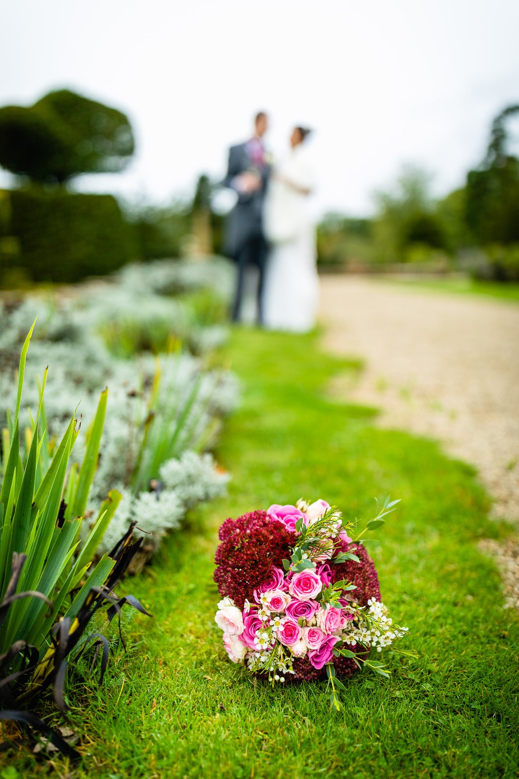 The bride's bouquet on the grass, the couple embracing along a garden path at Eynsham Hall
