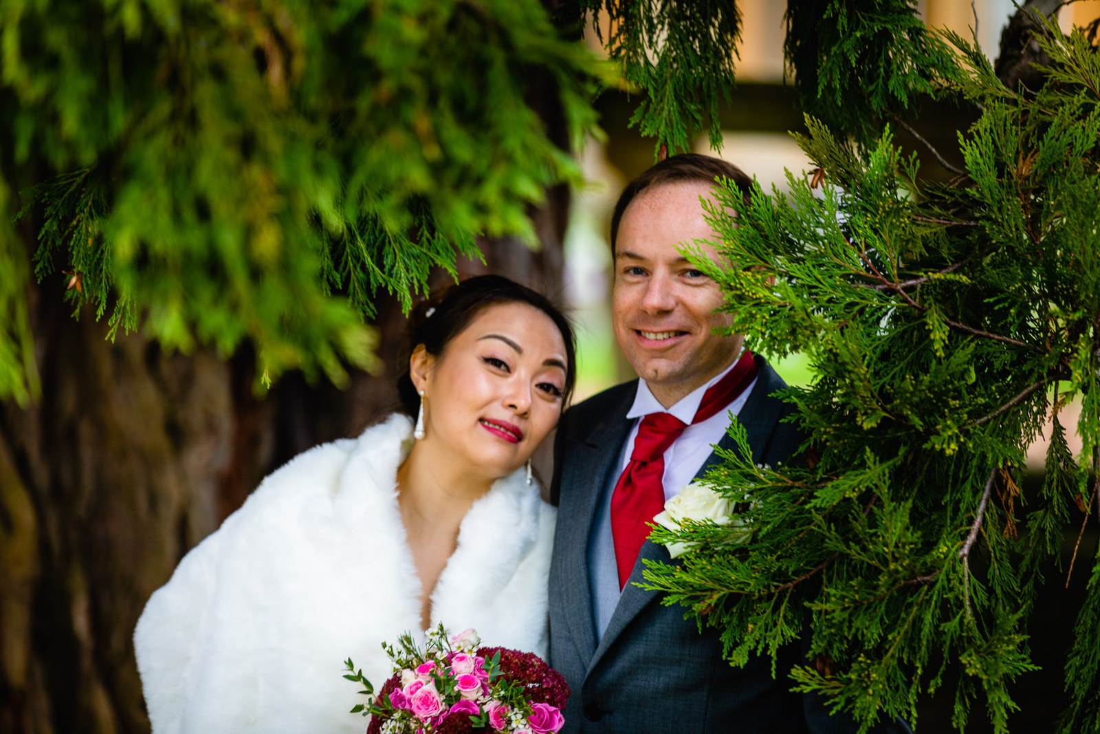 Bride and groom peeking around a cedar tree, the bride holding her bouquet