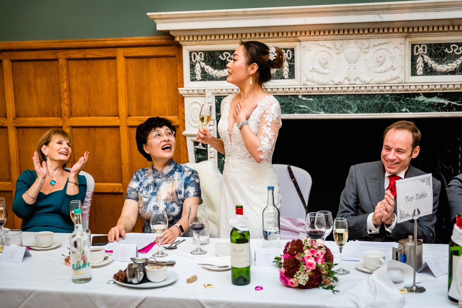 Bride rising to give a toast at the top table as guests applaud