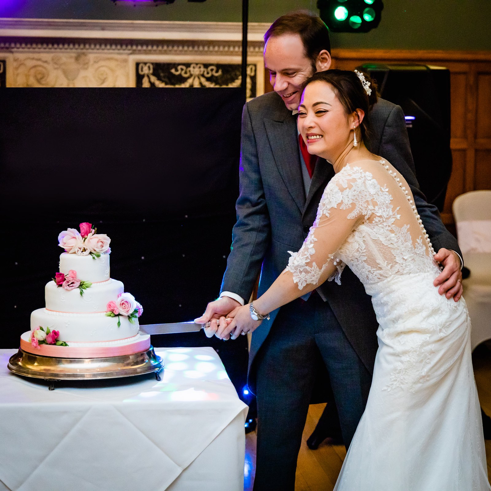 The couple cutting their three-tier cake together under coloured lights