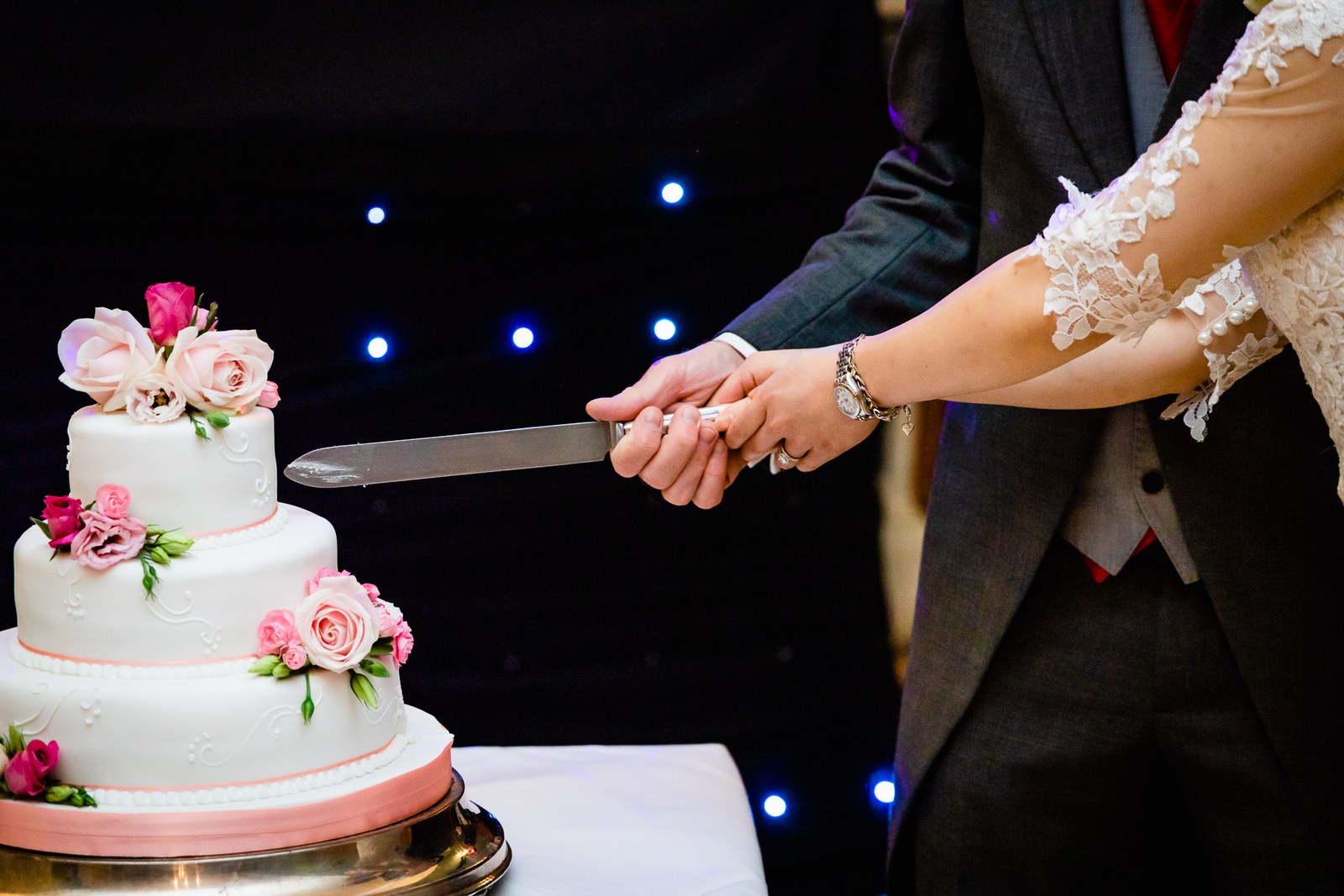 Close-up of the couple's hands guiding the knife into the wedding cake