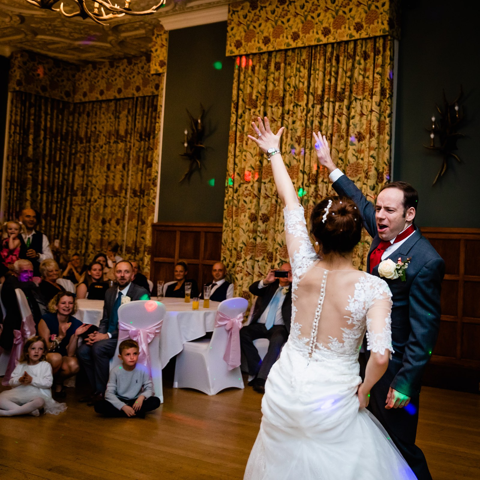 Bride and groom dancing with arms raised as seated guests look on