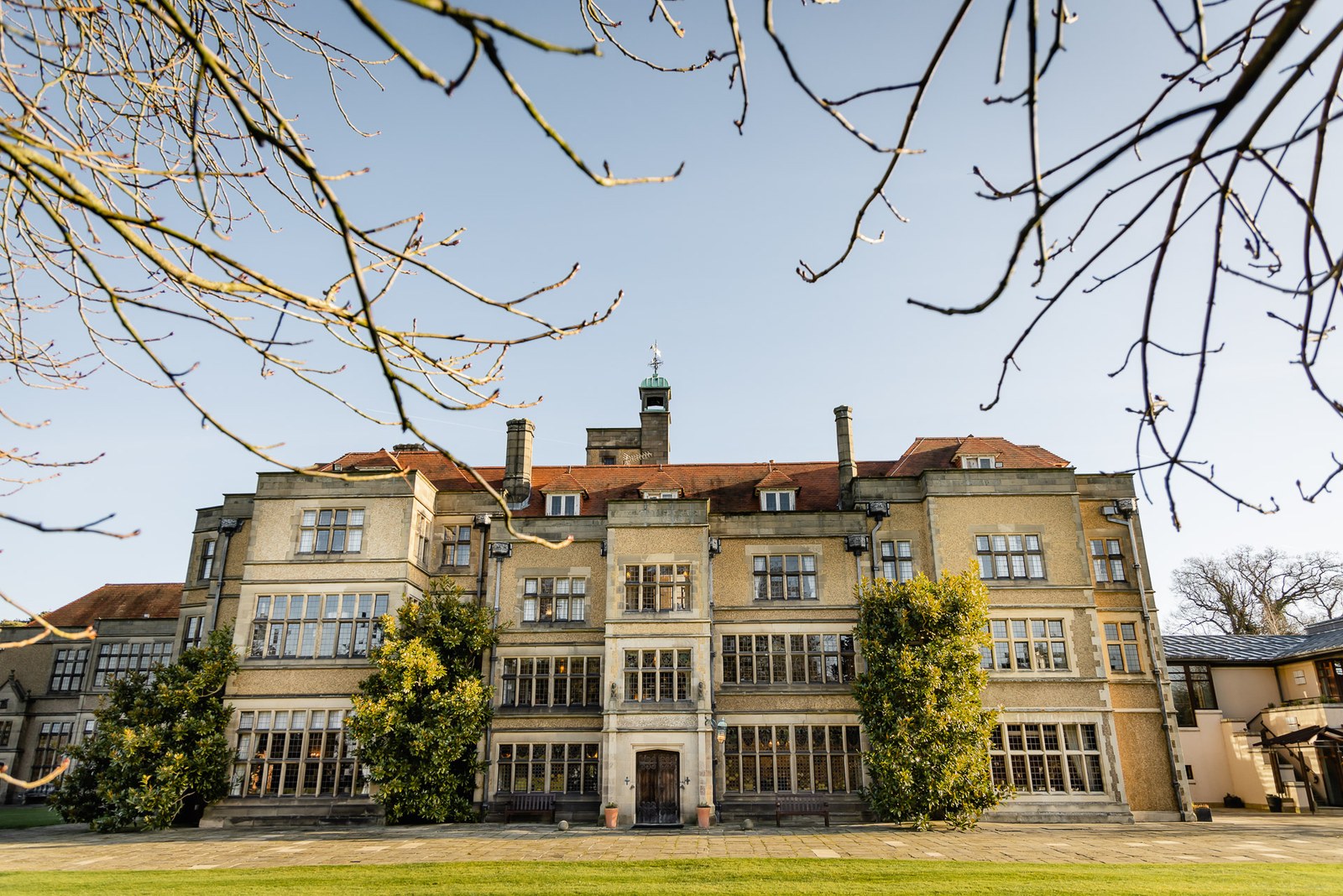 The Jacobean pale-stone facade of Fanhams Hall behind winter-bare trees and lawn