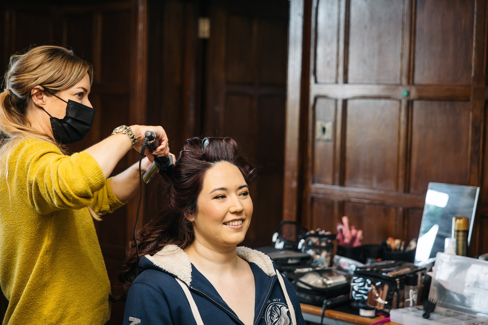 Hairstylist curling the bride's hair in an oak-panelled dressing room