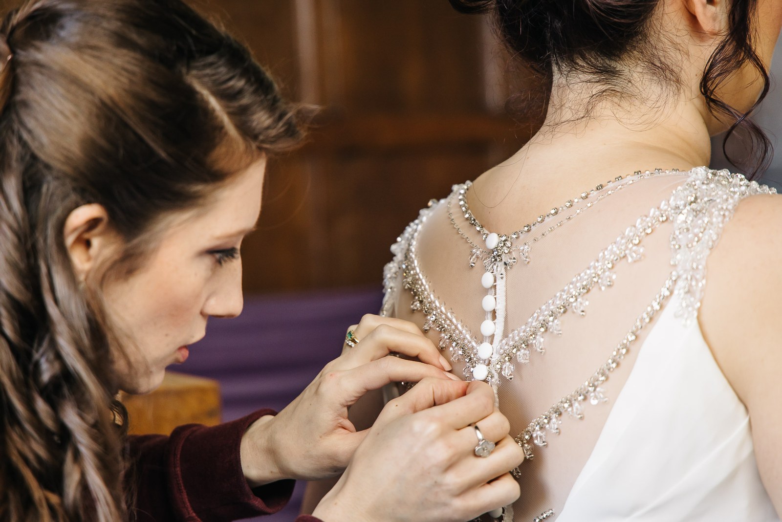 A helper fastening the small buttons at the back of the bride's beaded gown