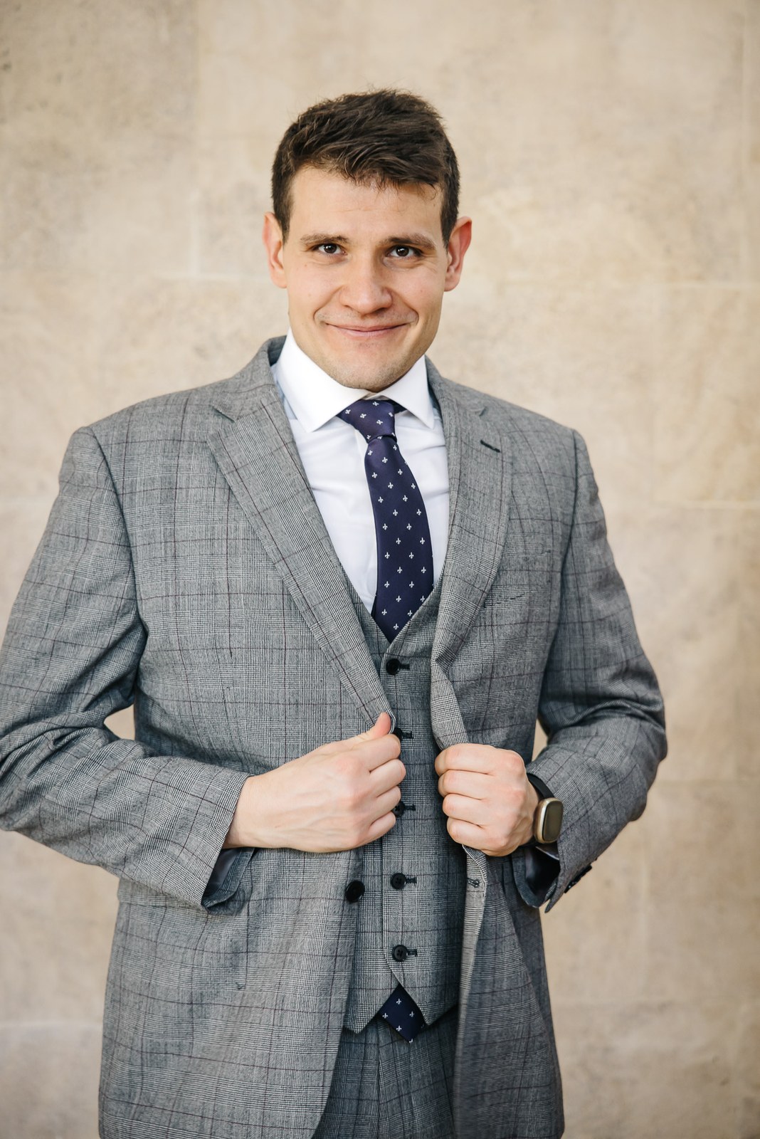 Groom buttoning his checked waistcoat for a portrait against a plain wall