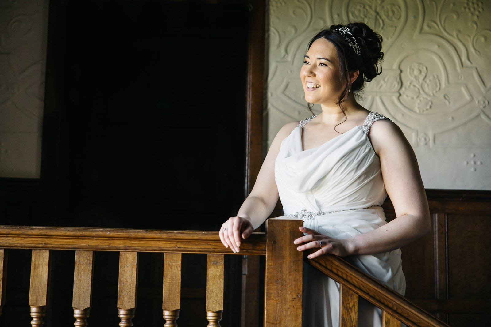 Bride smiling on the oak staircase of Fanhams Hall against an ornate plaster wall