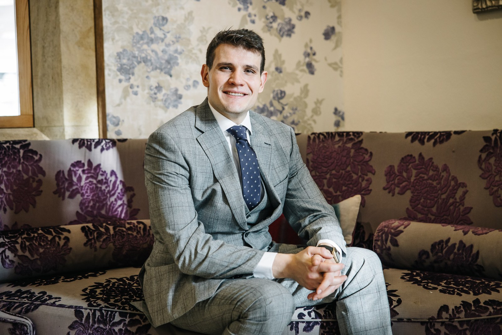 Groom waiting on a floral-patterned sofa, hands clasped, before the ceremony