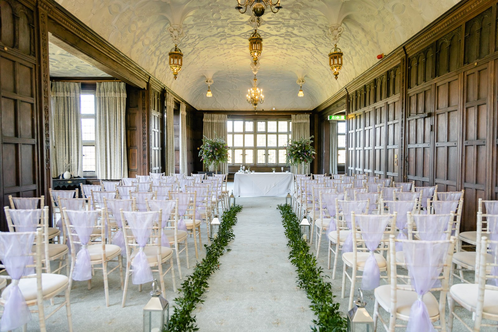 The Long Gallery at Fanhams Hall set for the ceremony, a foliage-lined aisle beneath a plaster ceiling
