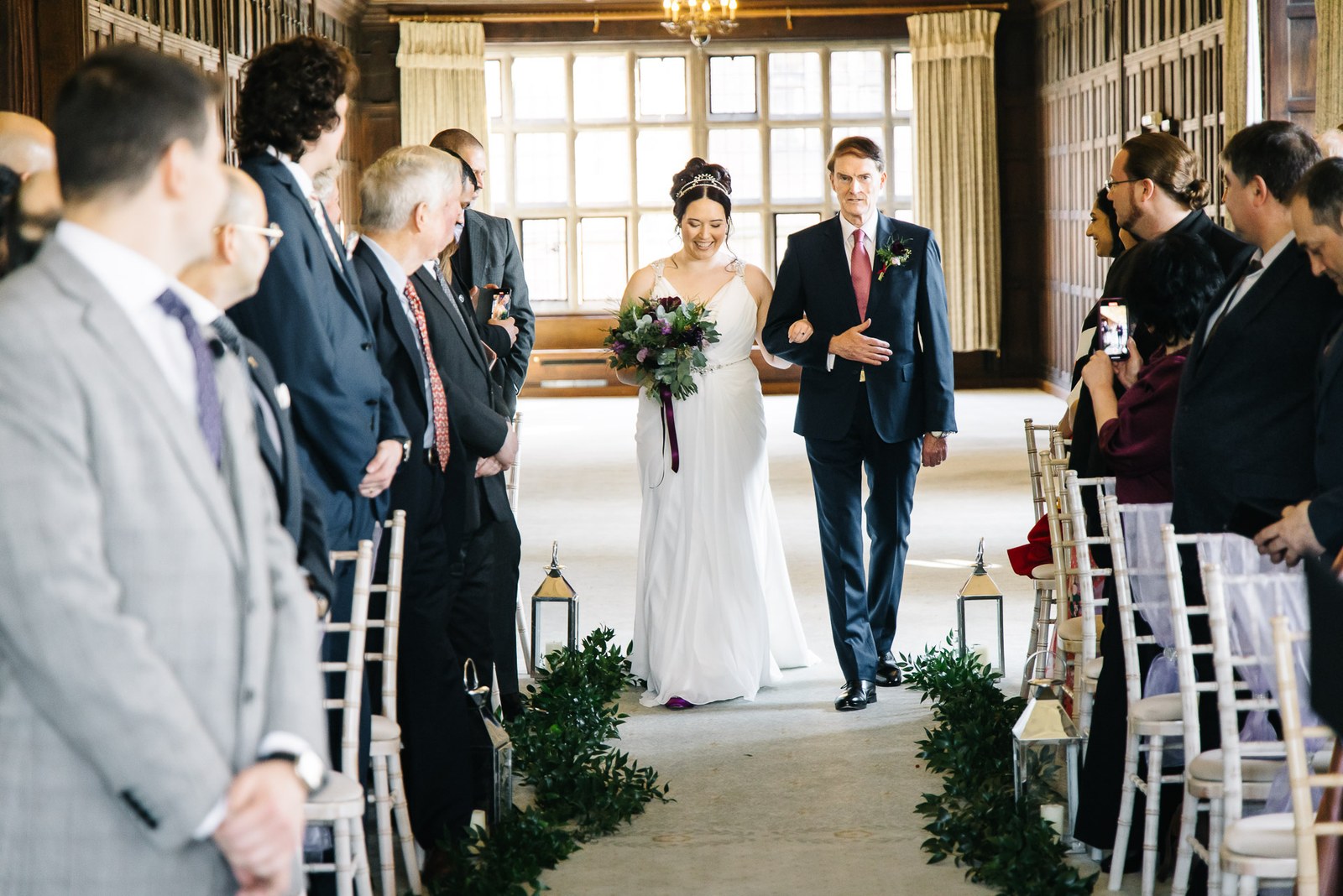 Bride walking down the foliage-lined aisle on an escort's arm as guests stand