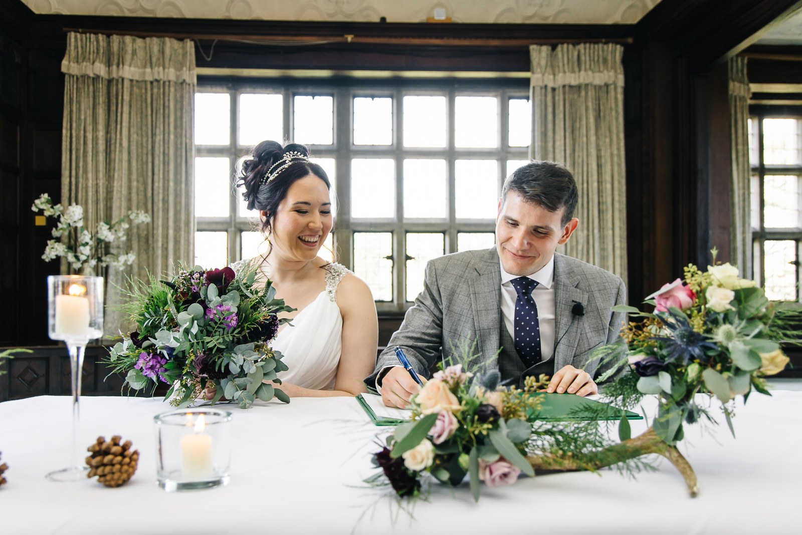 Signing the register at a candlelit table dressed with flowers by a leaded window