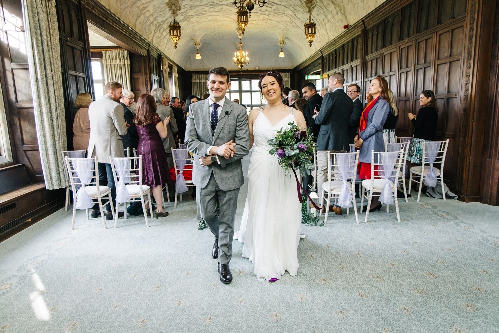 Newlyweds walking back down the aisle through the panelled gallery at Fanhams Hall