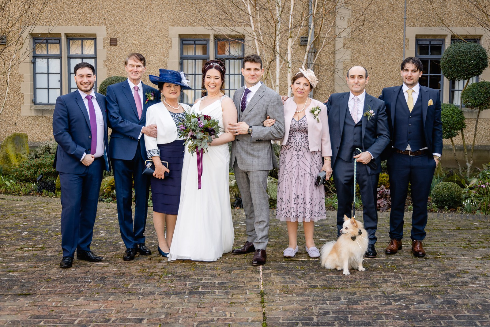 Family group before the pale stone facade of Fanhams Hall, a small dog at their feet