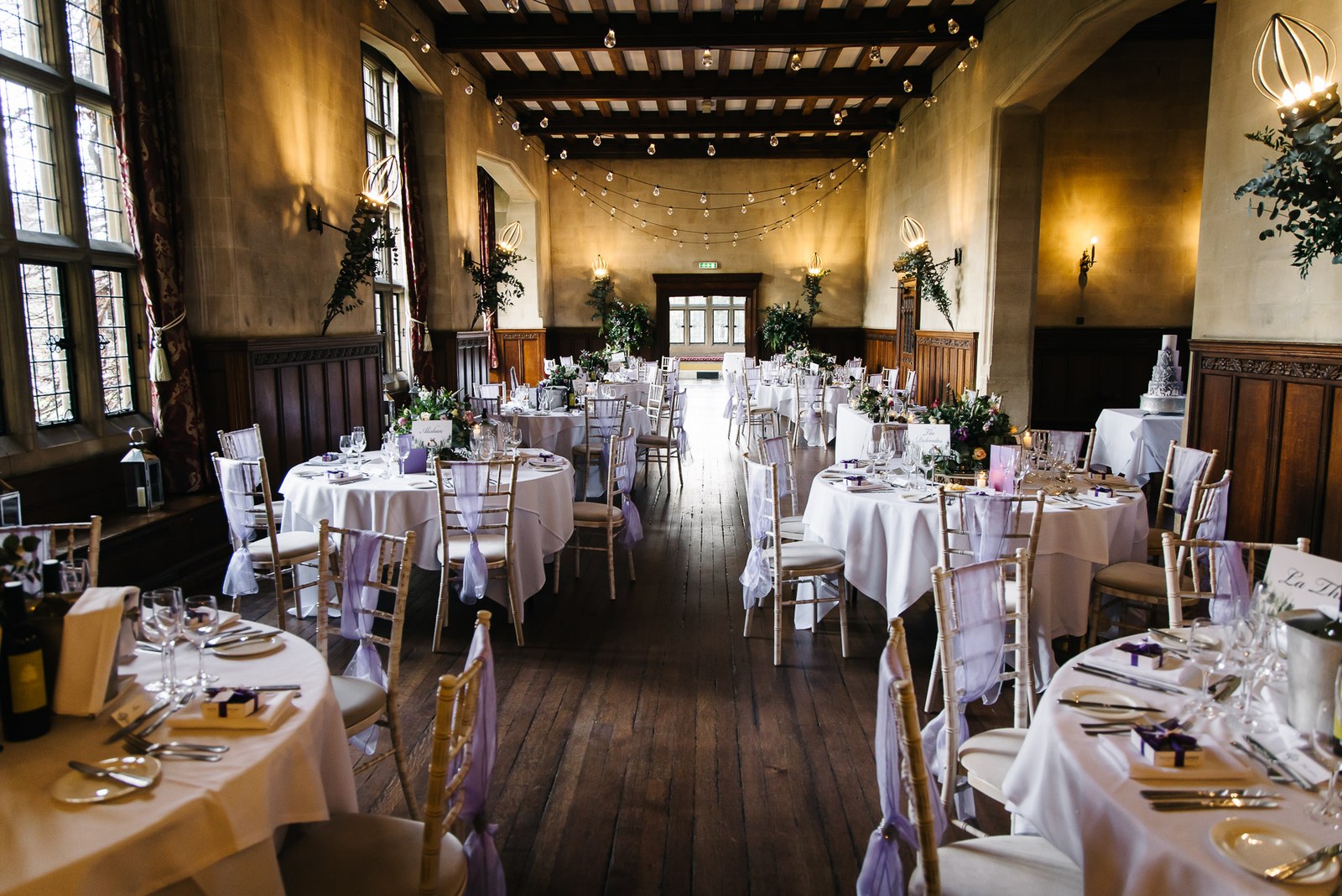 The dining hall at Fanhams Hall laid with round tables beneath a timber-beamed ceiling