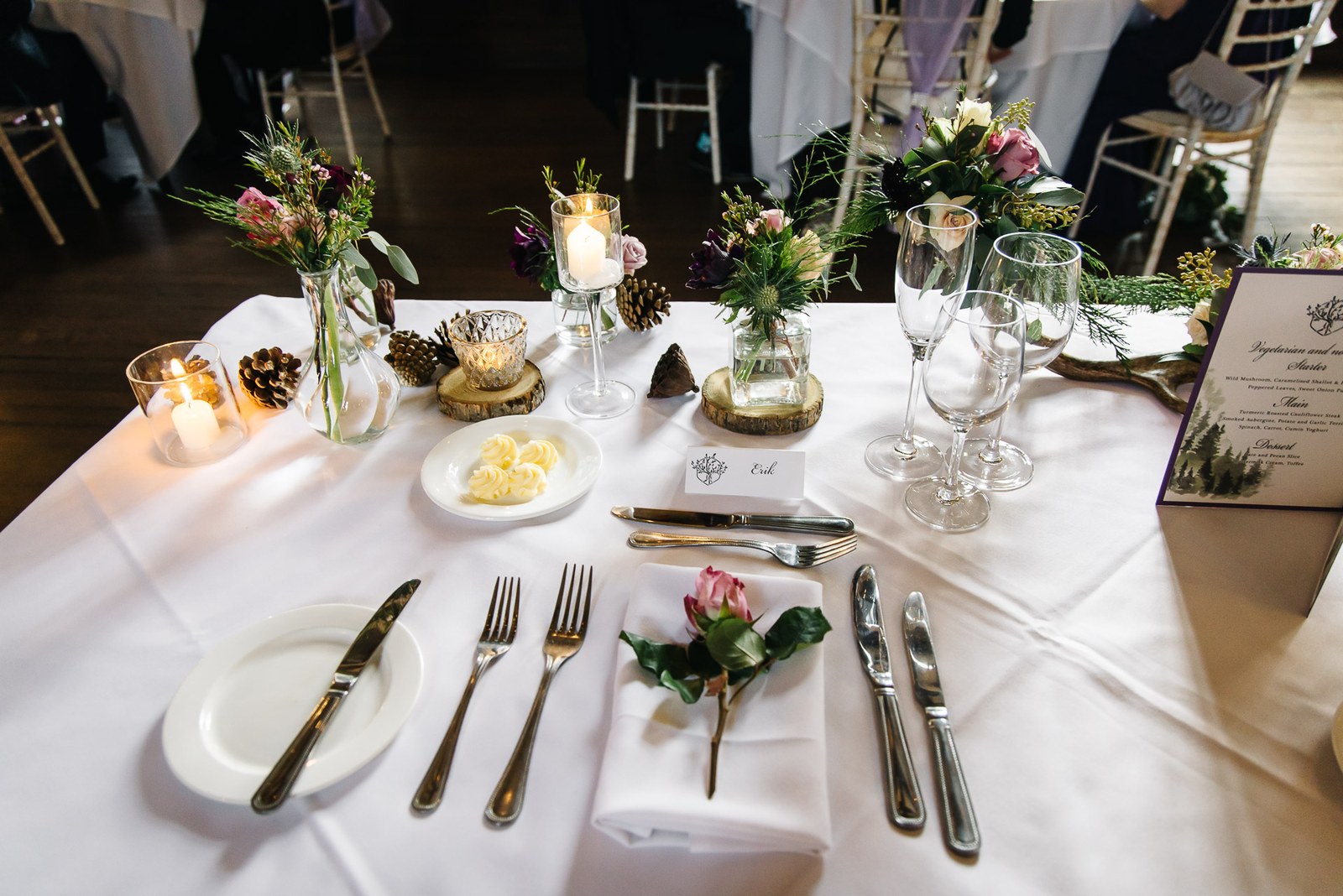 Close-up of a sweetheart-table place setting with candles, pinecones and a single rose