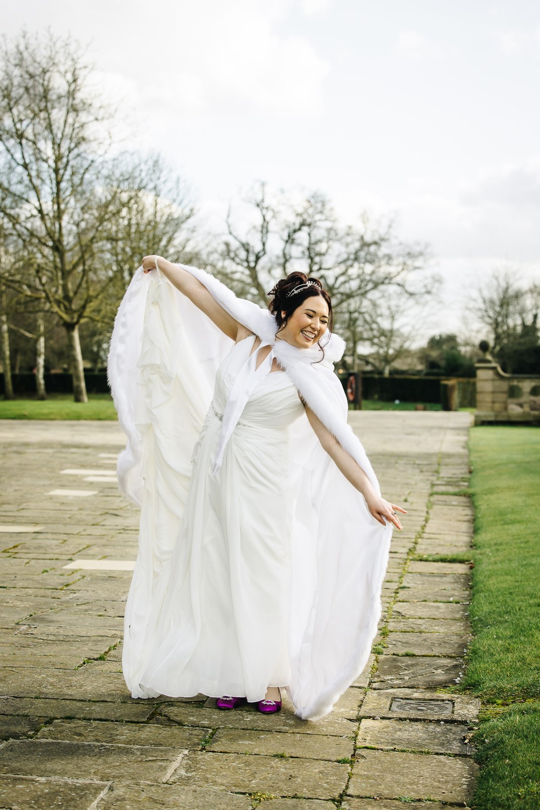 Bride swishing her cloak on the garden terrace at Fanhams Hall among bare winter trees