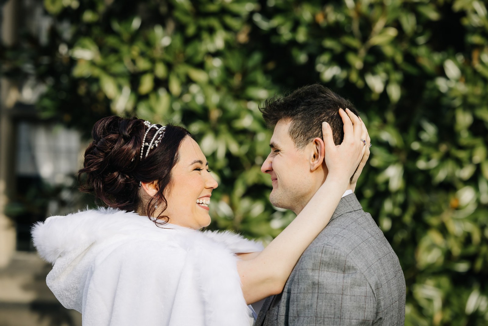 Bride and groom embracing among glossy evergreen leaves, the bride in a fur cape