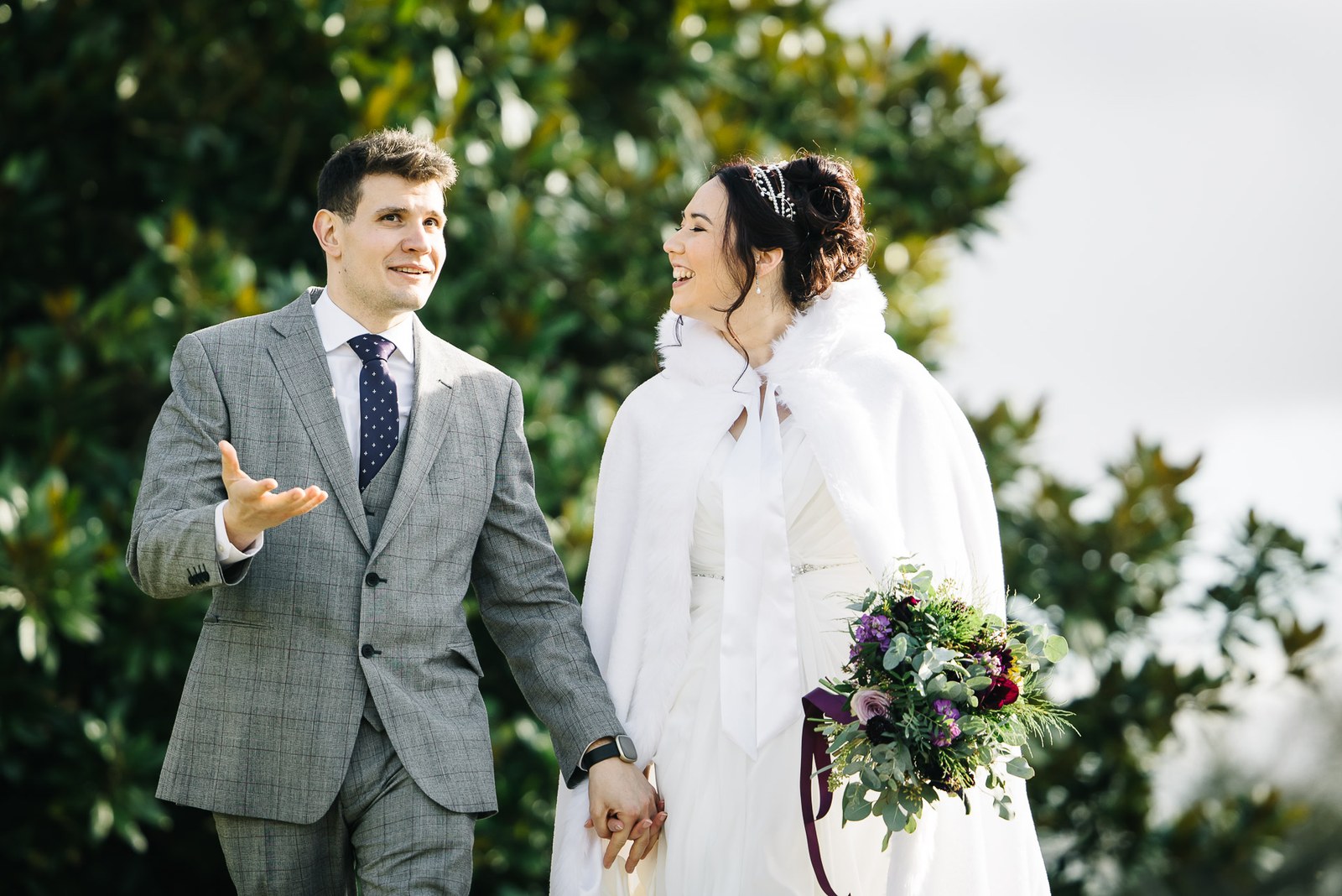 Bride and groom walking hand in hand through the greenery, bouquet in hand
