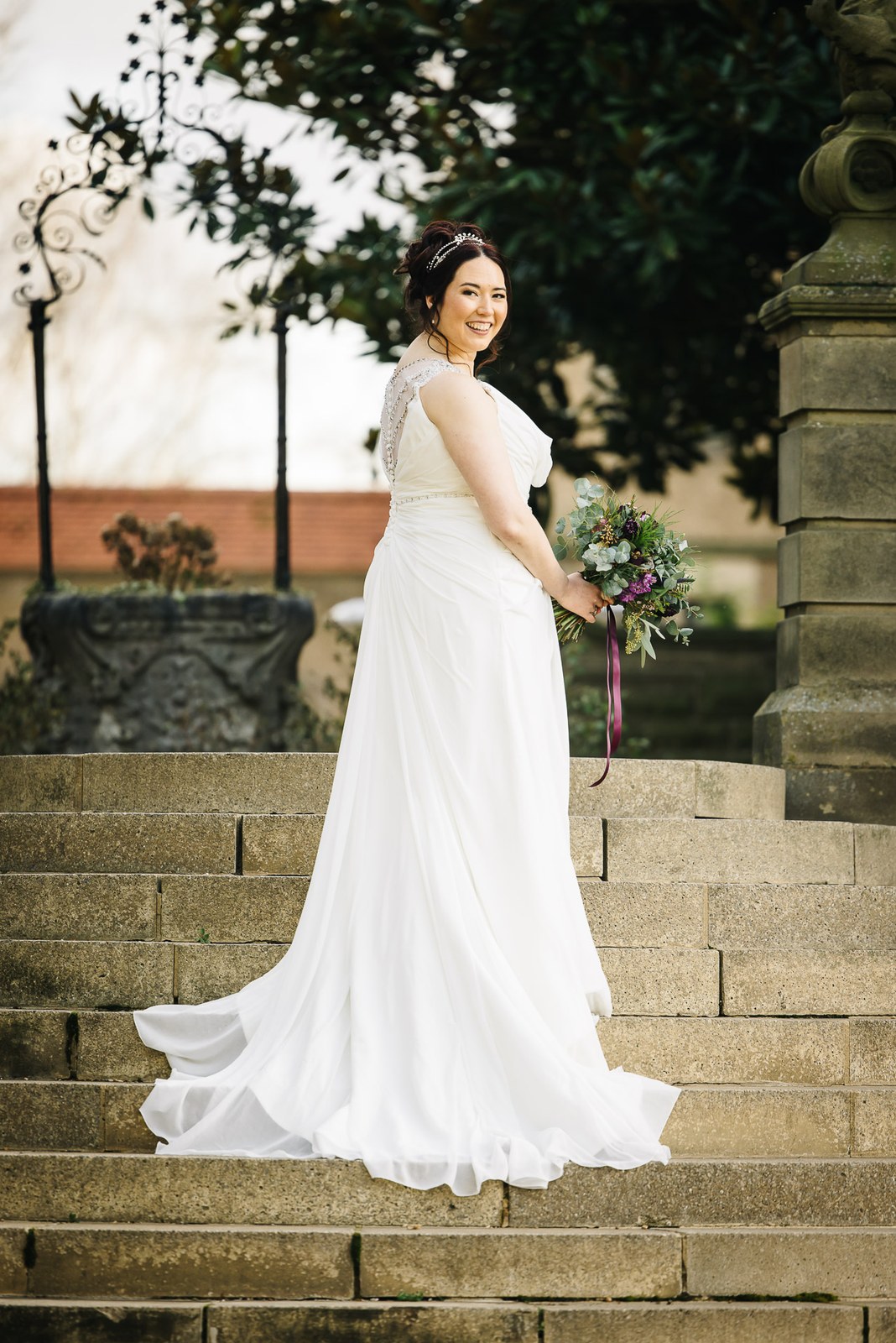 Bride posing with her train draped down the stone garden steps at Fanhams Hall