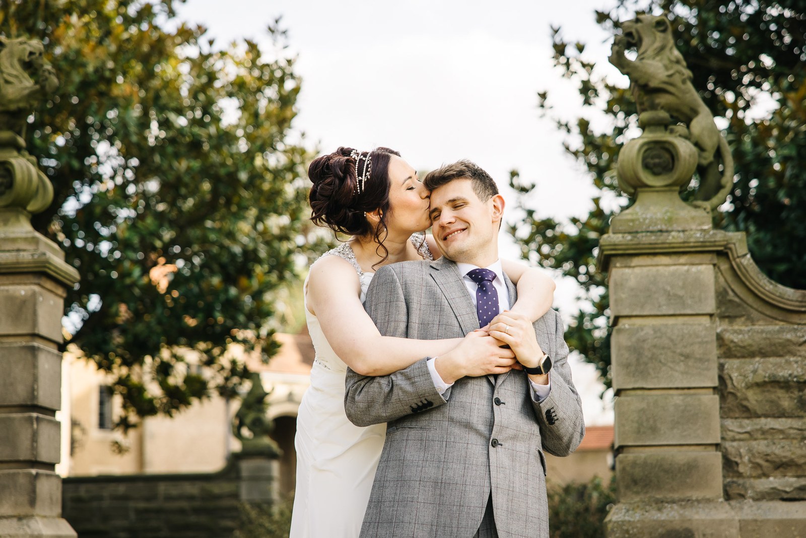 Bride kissing the groom's temple between stone gate piers topped with heraldic beasts