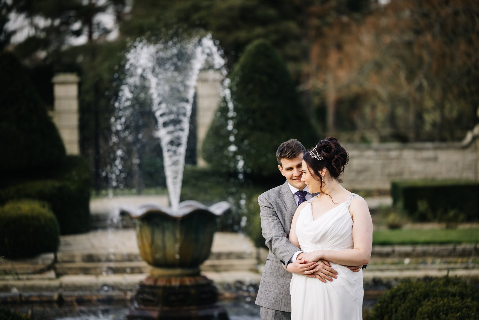 The couple embracing beside an ornamental fountain in the formal gardens of Fanhams Hall