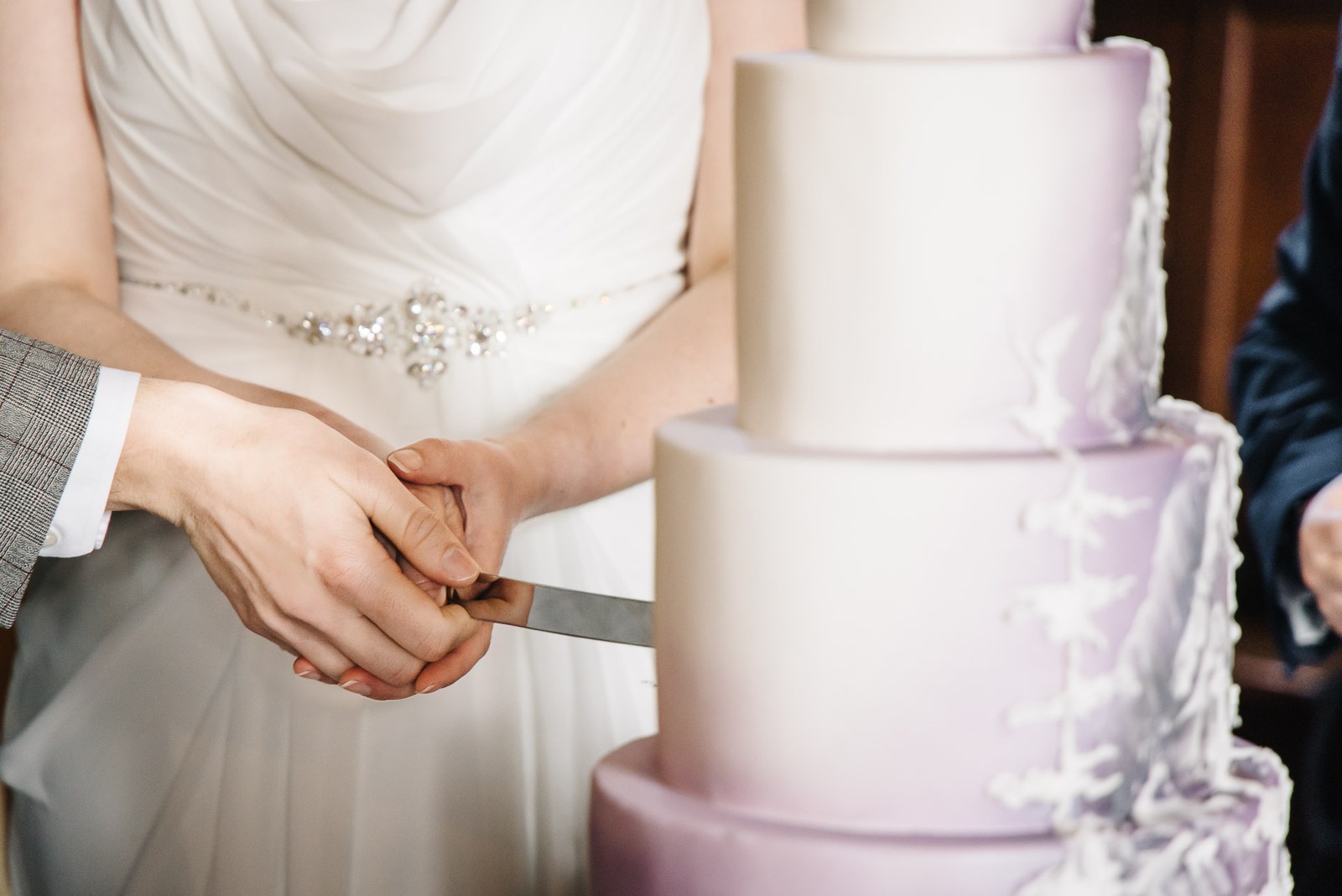 Close-up of the couple's hands cutting their tiered lilac wedding cake