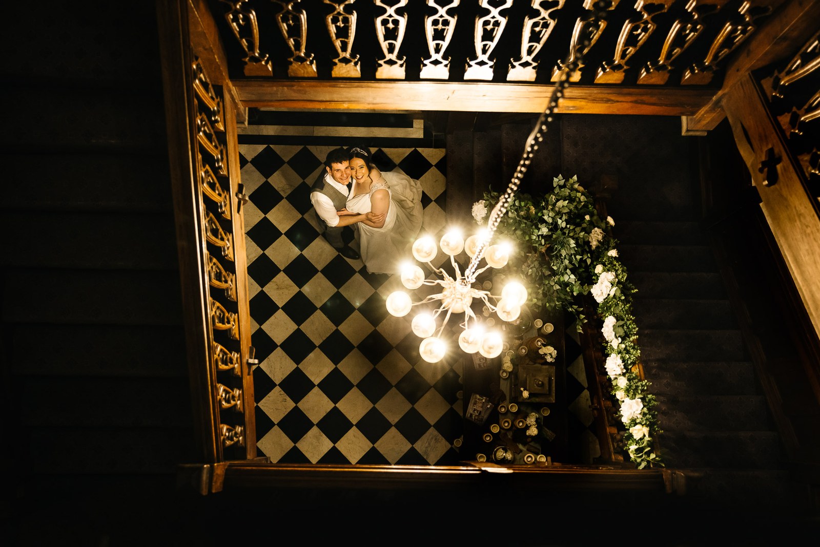 Overhead night view of the couple embracing on the chequerboard floor beneath a chandelier at Fanhams Hall