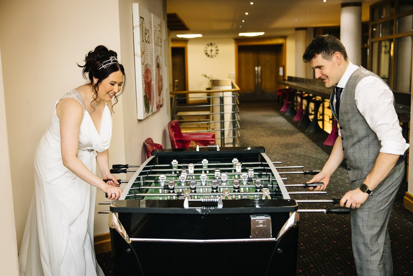 Bride and groom laughing over a game of table football in the corridor