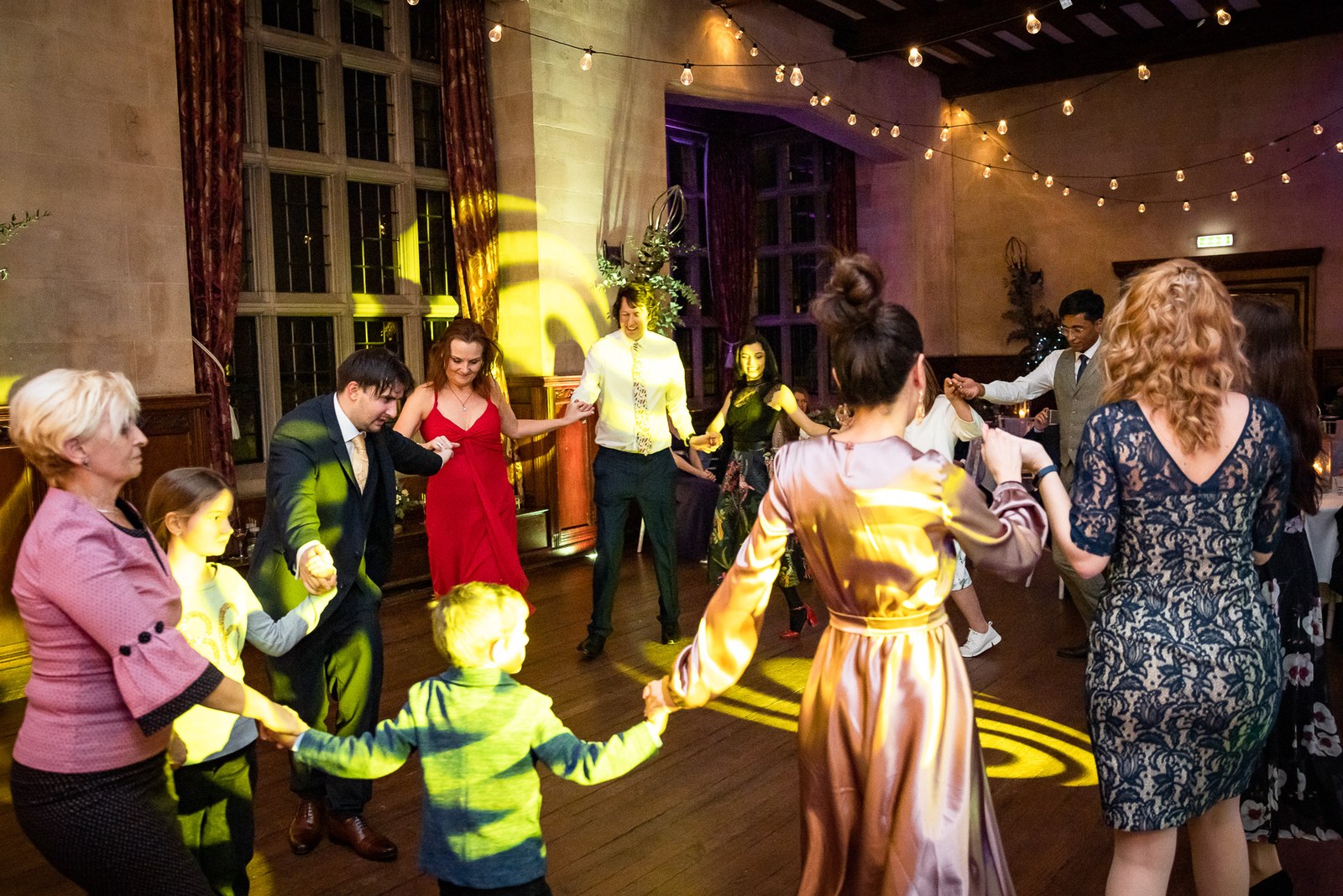 Guests dancing in a joined-hands circle under strings of festoon lights