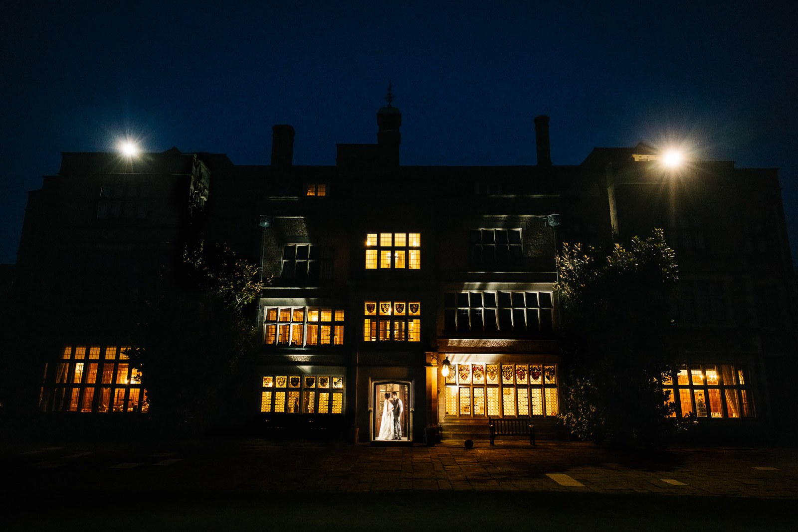 Fanhams Hall floodlit at night, the couple framed in a warmly lit doorway