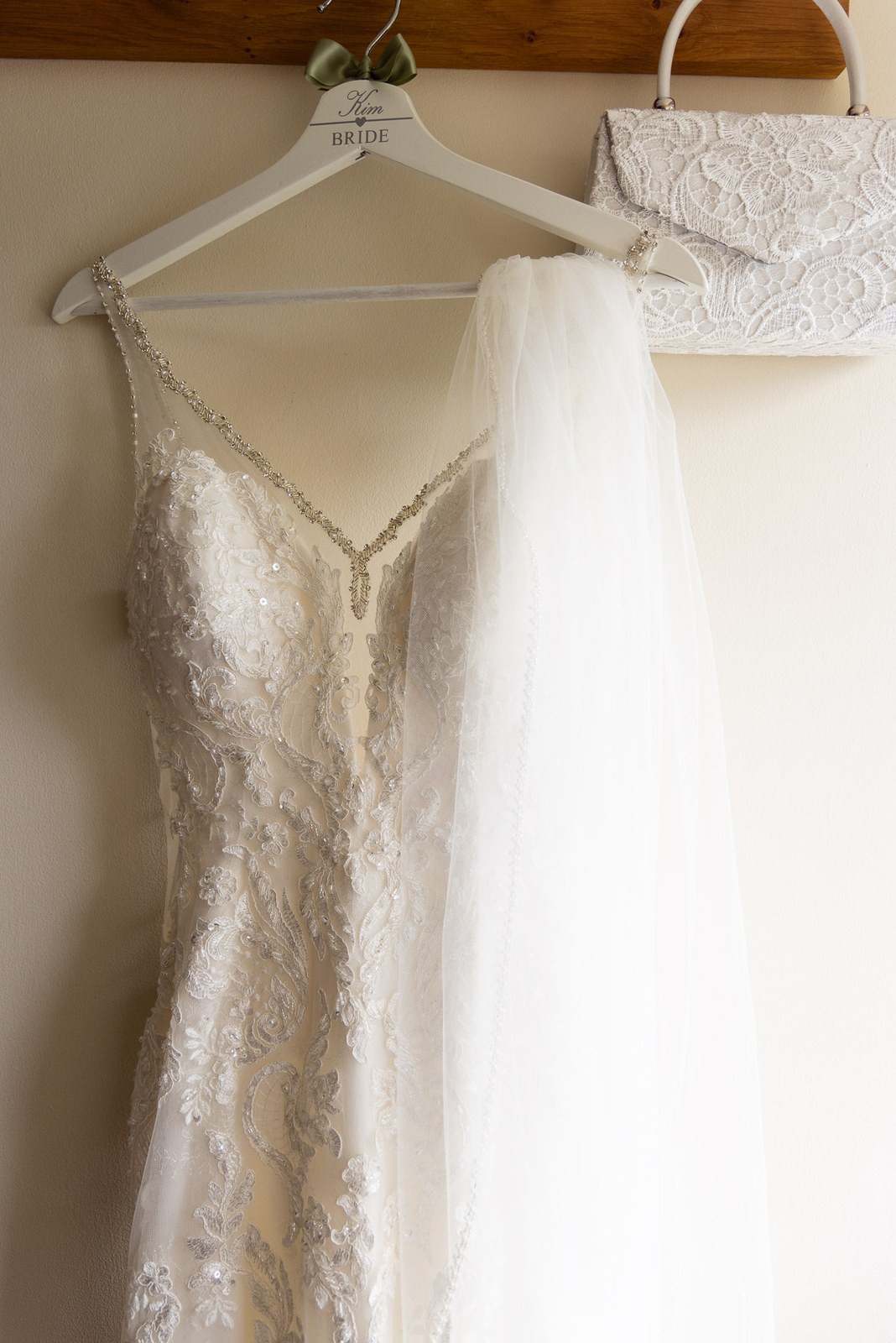 The beaded lace wedding gown and veil on a 'Bride' hanger beside a lace clutch