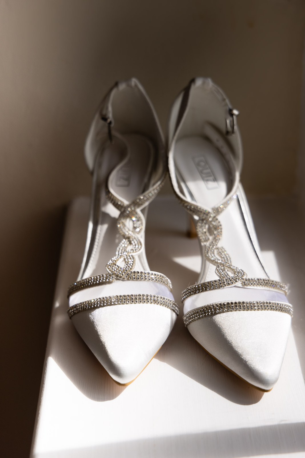 A pair of white satin bridal heels with diamante straps catching the light