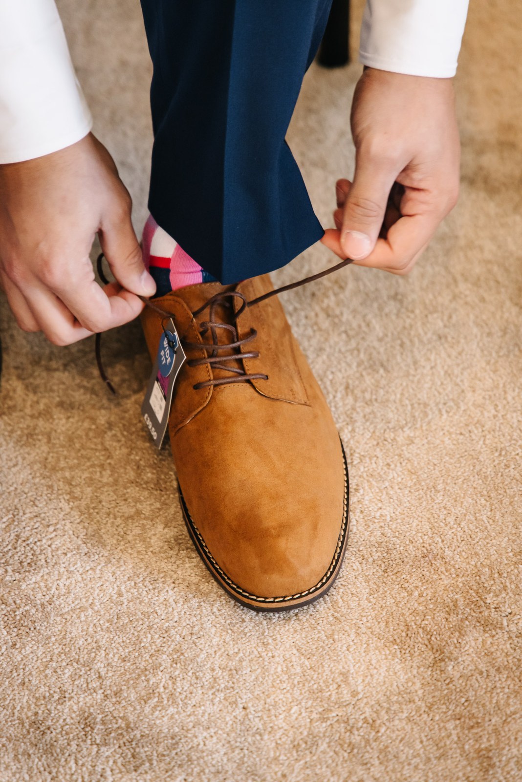 A groomsman lacing up his tan suede shoes