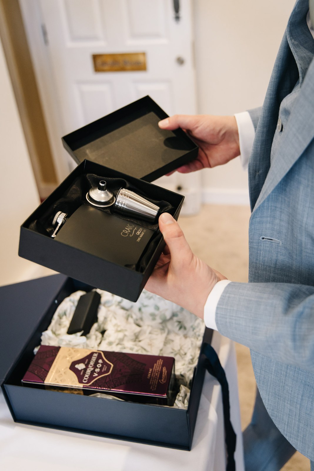 The groom opening a gift box holding a hip flask and keepsakes