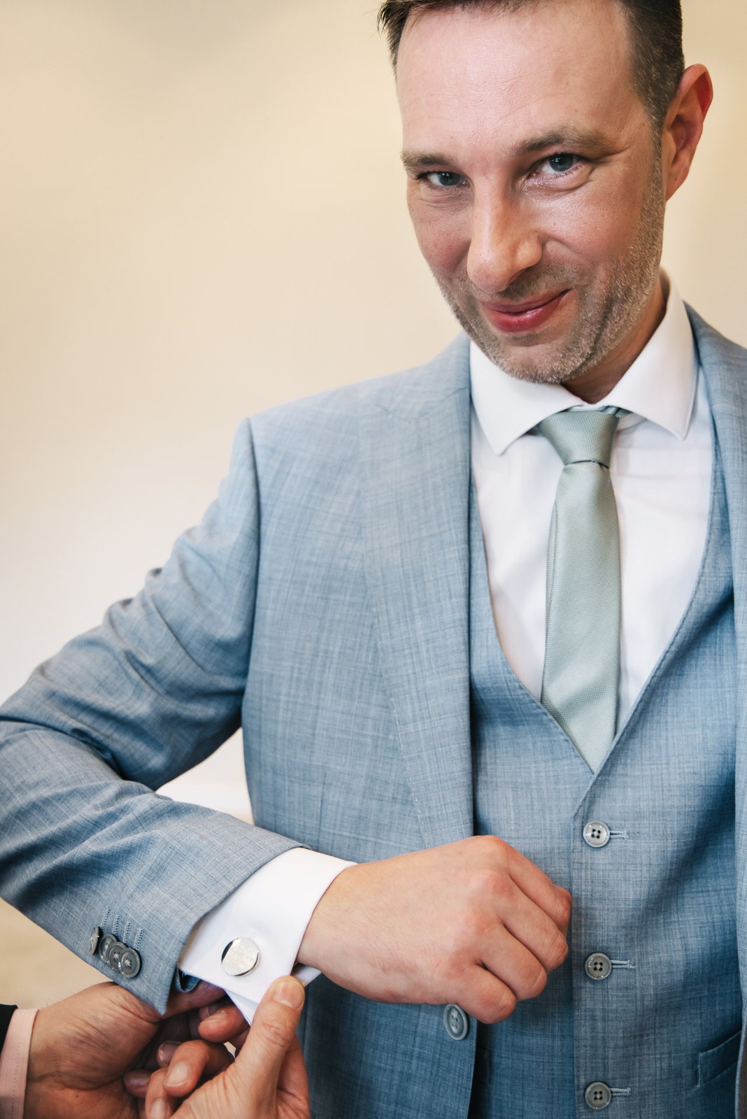 Groom in a pale blue three-piece suit fastening a cufflink