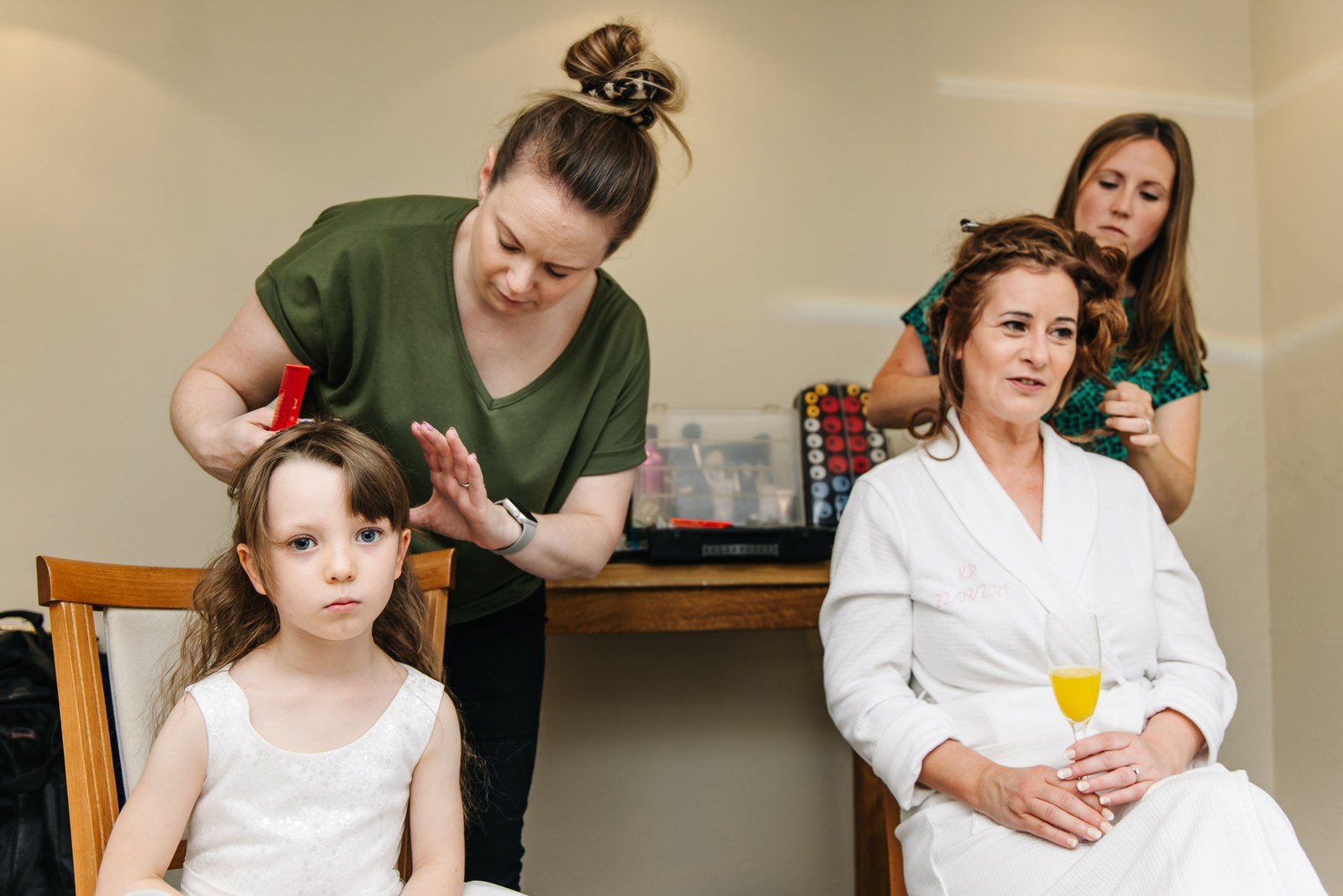 Hairstylist styling hair as a flower girl waits during the morning preparations