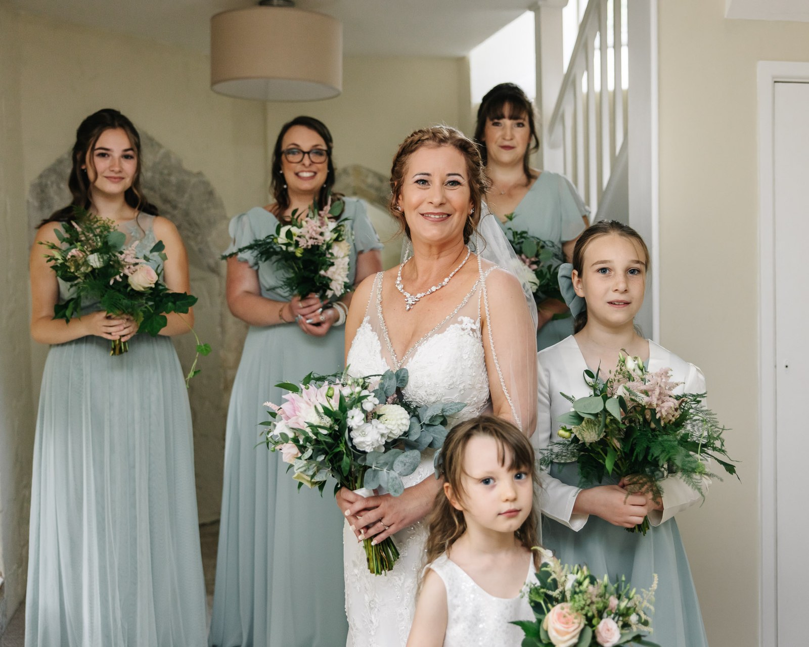 The bride with her bridesmaids and flower girls, all holding soft pastel bouquets