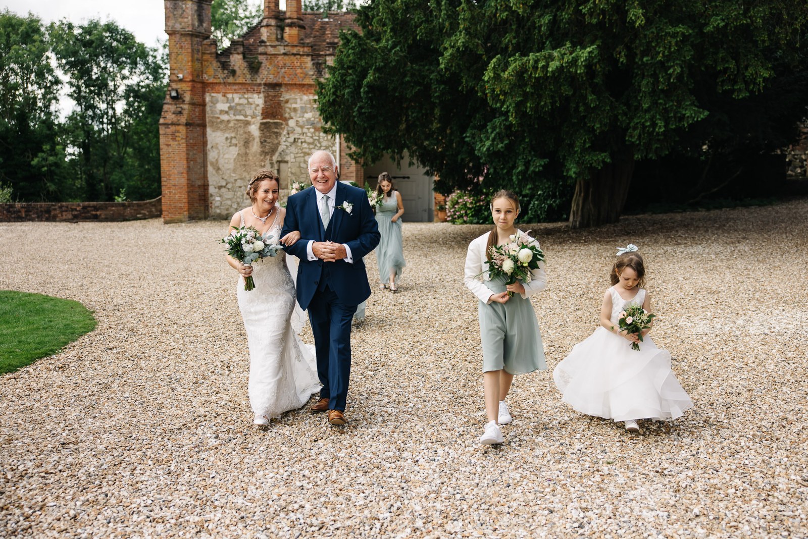 The bride walking the grounds on her father's arm, the tower of Farnham Castle behind