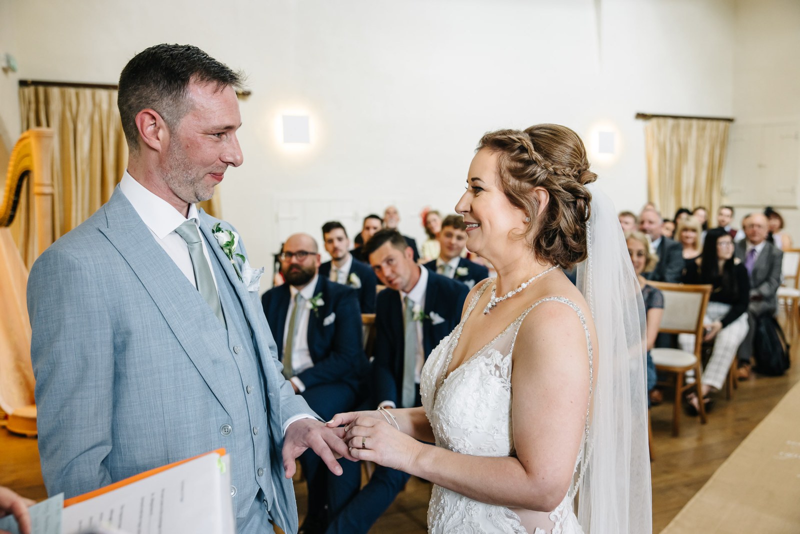 The bride sliding the ring onto the groom's finger as guests watch