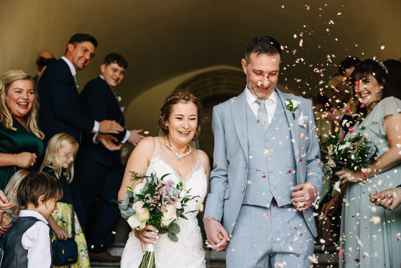 Newlyweds showered with confetti beneath a stone archway at Farnham Castle