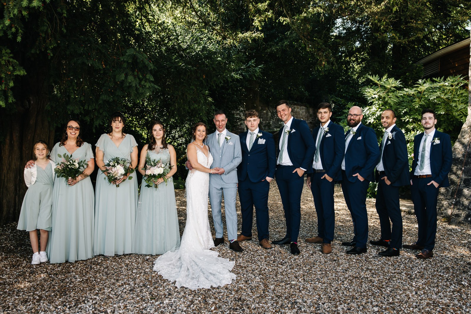 The full bridal party lined up on the gravel beneath leafy trees