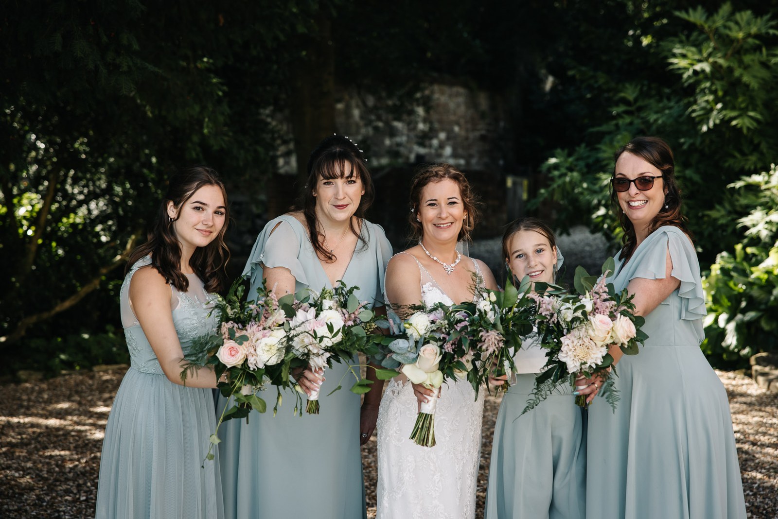 The bride with her bridesmaids holding lush pastel bouquets in the sunshine