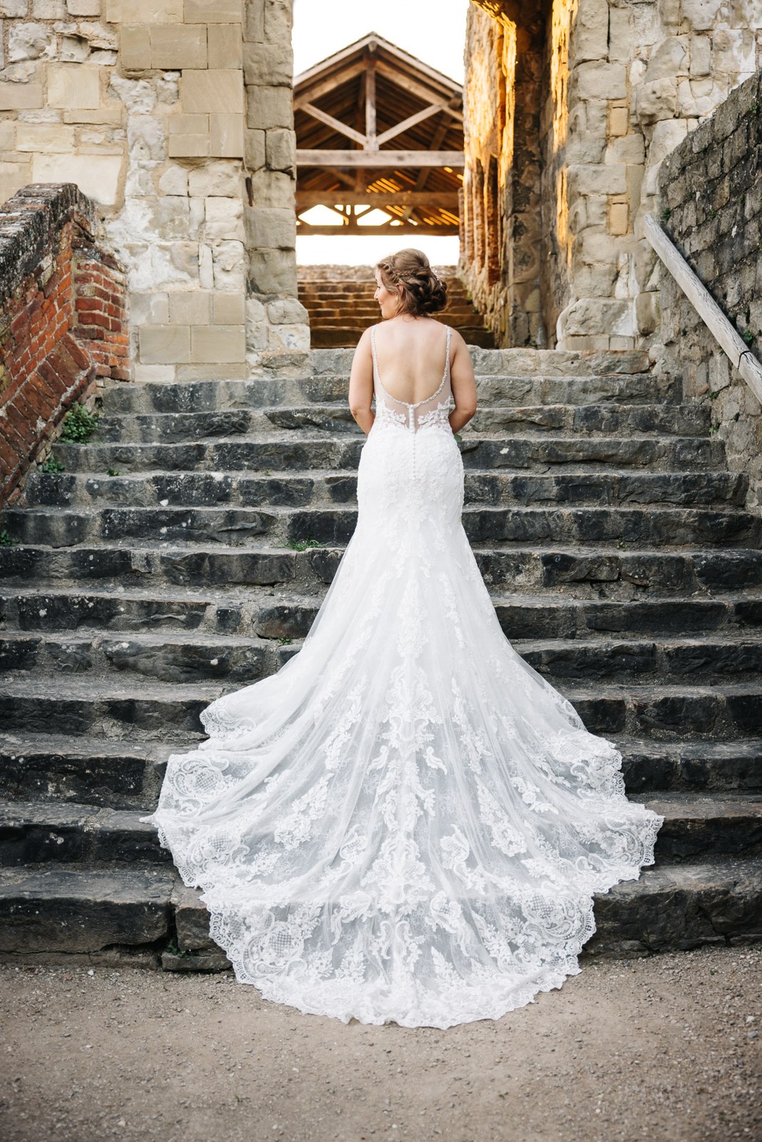 The bride on the ancient stone steps of Farnham Castle, her lace train fanned out