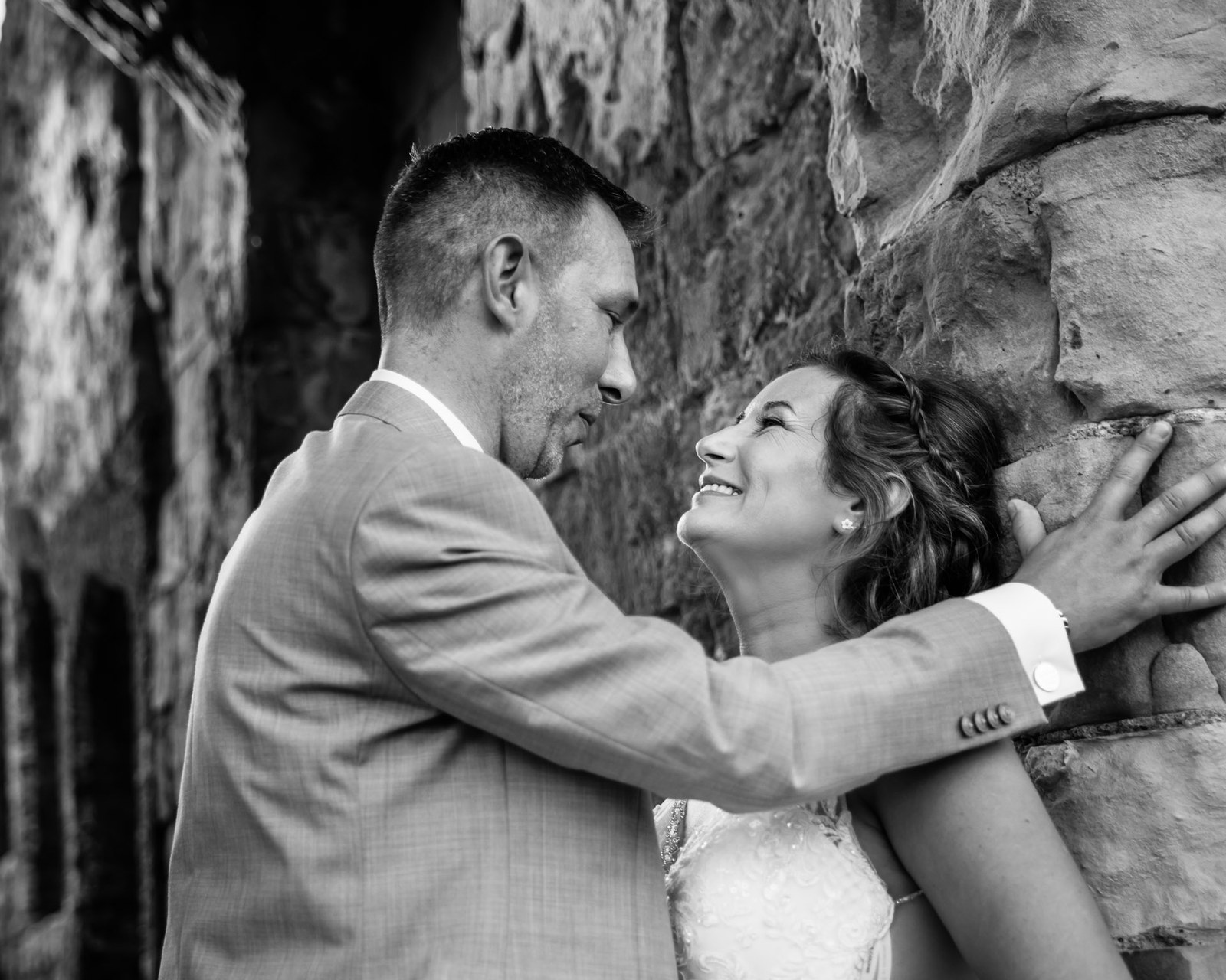 Black-and-white of the couple embracing against the rough stone wall of Farnham Castle