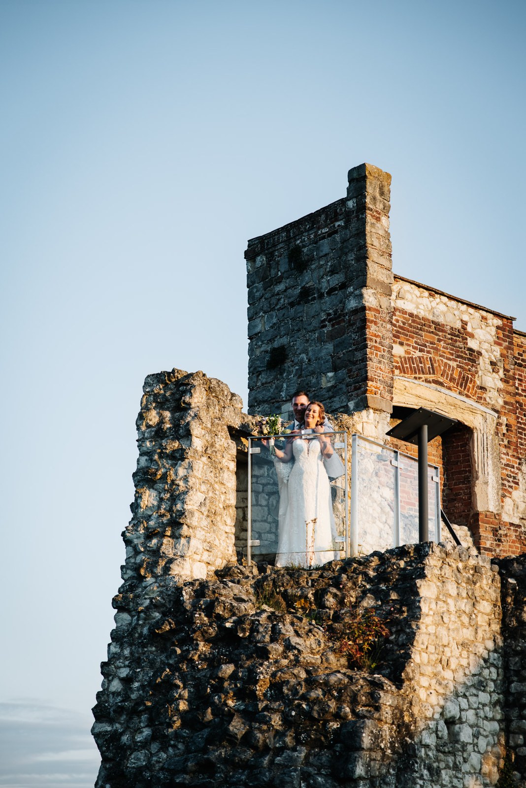 The couple tiny on the ruined keep of Farnham Castle against a clear evening sky